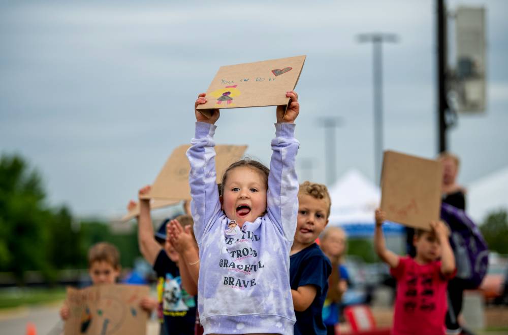 Young girl from the GVSU Children's Enrichment Center holding her "You can do it" handmade sign high in the air above her head, with her tongue sticking out
